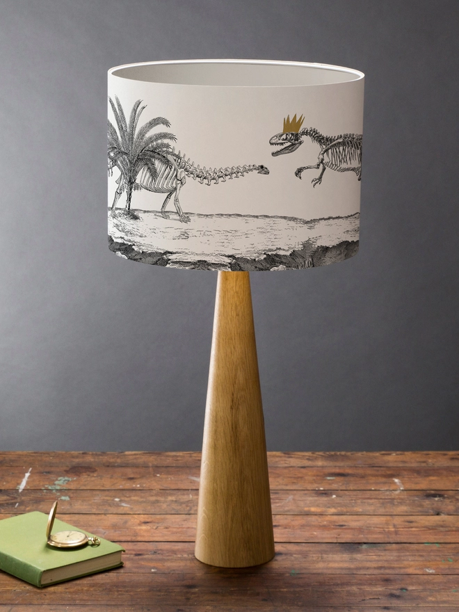 Drum Lampshade featuring Dinosaurs on a wooden base on a shelf with books and ornaments
