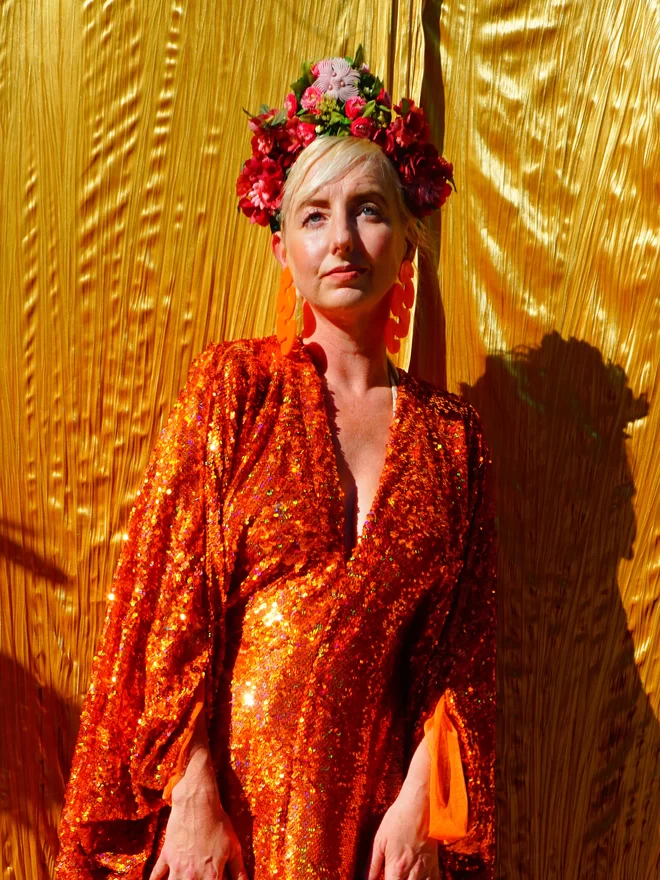 Close up of a woman wearing the orange sequin v-neck kaftan.