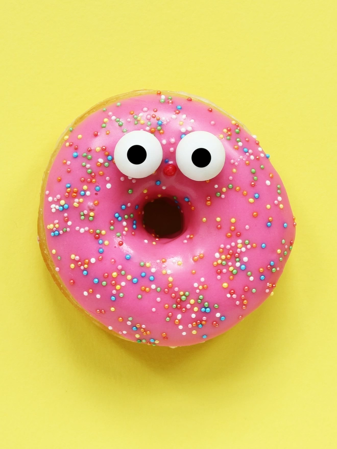 A surprised pink glazed doughnut on a zingy yellow backdrop