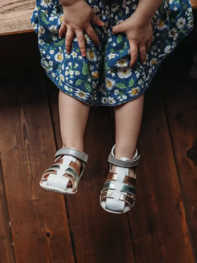 Little girl wearing a floral dress and Pip and Henry blue metallic gladiator sandals