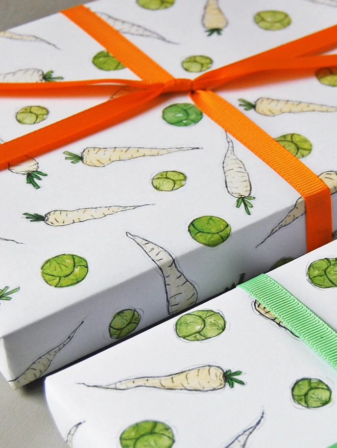 Two gifts wrapped in fun illustrated sprouts and parsnips wrapping paper is tied with orange ribbon.