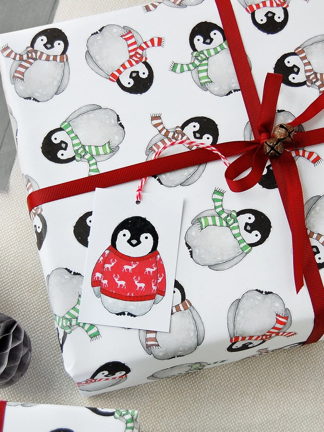 A gift is wrapped in wrapping paper with an illustrated baby penguin design, and red ribbon tied around it.