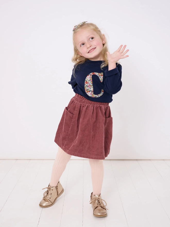 A navy cotton long sleeve t-shirt appliquéd with an initial in a floral Liberty print, worn by a 4 year old girl