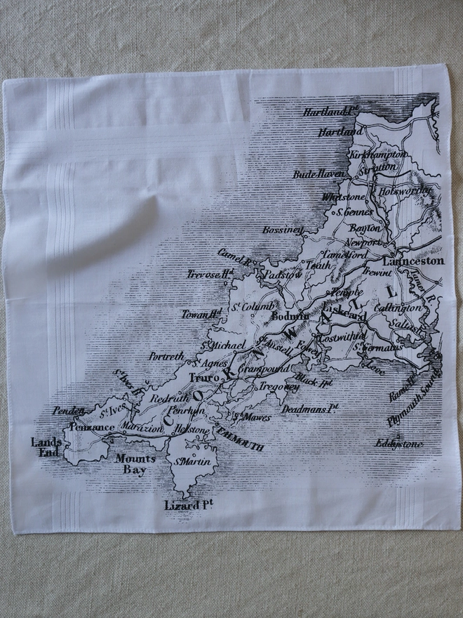 A Mr.PS Cornwall map hankie printed in black laid flat on a linen tablecloth