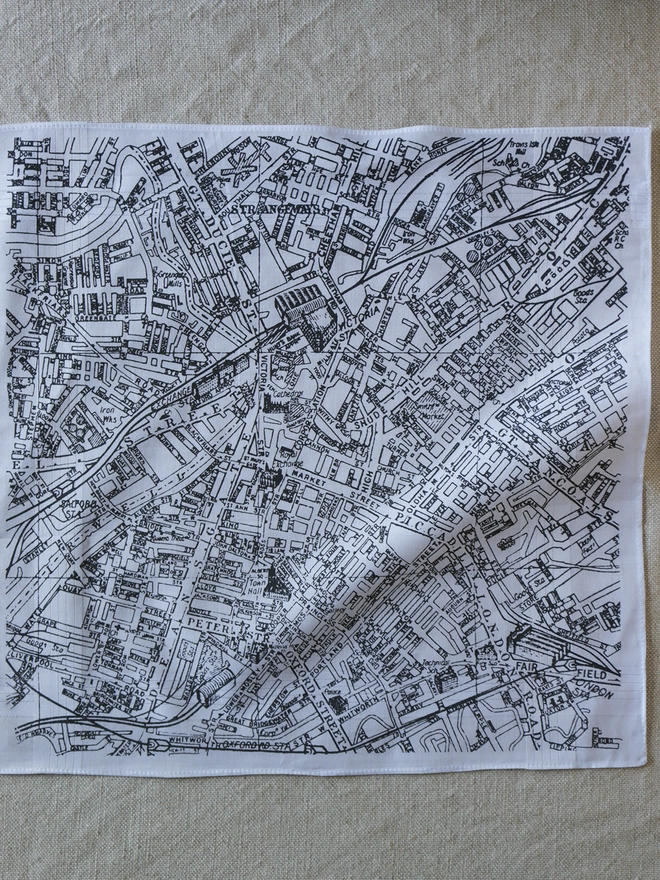 A Mr.PS Manchester map hankie printed in grey laid flat on a linen tablecloth