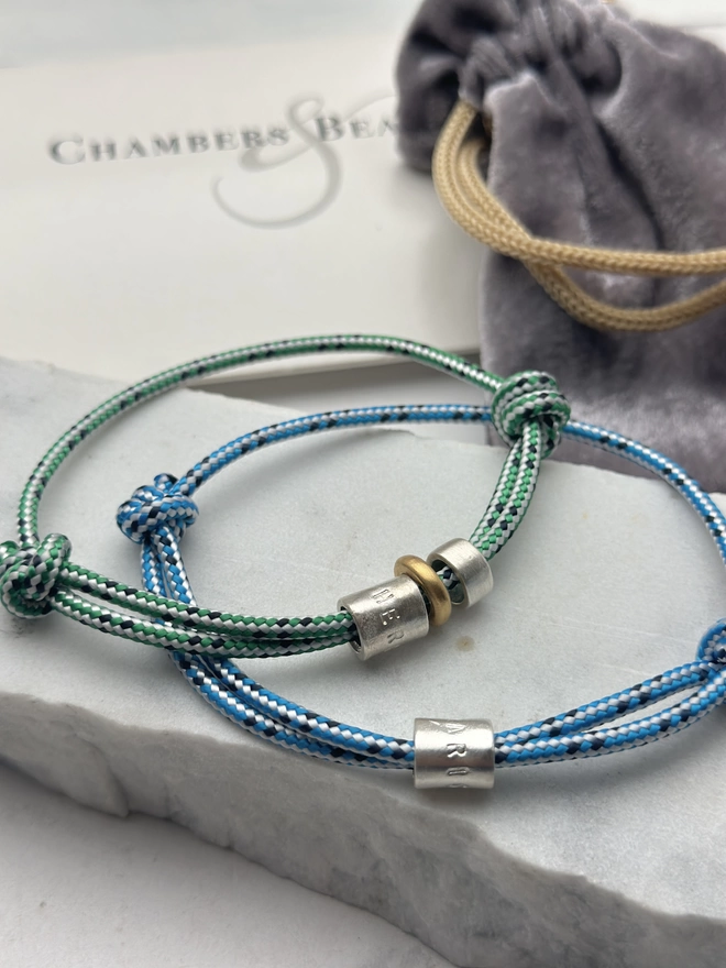men's personalised sterling silver bead friendship bracelets. one on blue, the other on green cord. gift pouch and box in the background