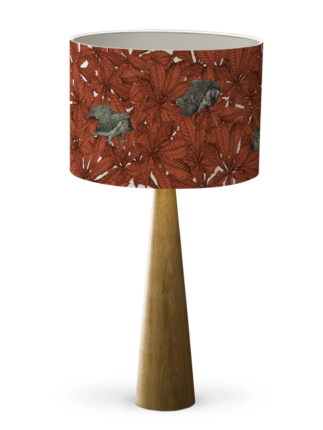Drum Lampshade featuring hedgehogs in autumnal russet red leaves with a white inner on a wooden base on a white background