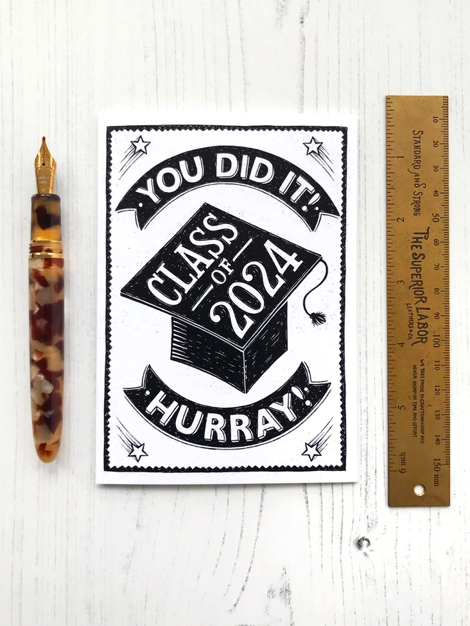black and white class of 2024 graduation card with tortoiseshell fountain pen and brass ruler
