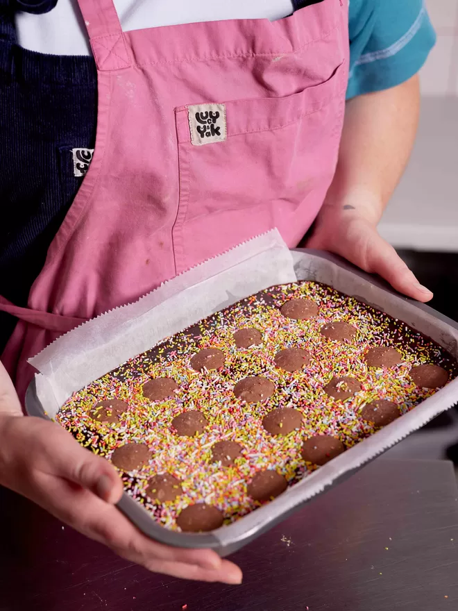 Oven ready tray of Funfetti brownies being held in a baking tray by Founder Hetty in the bakery