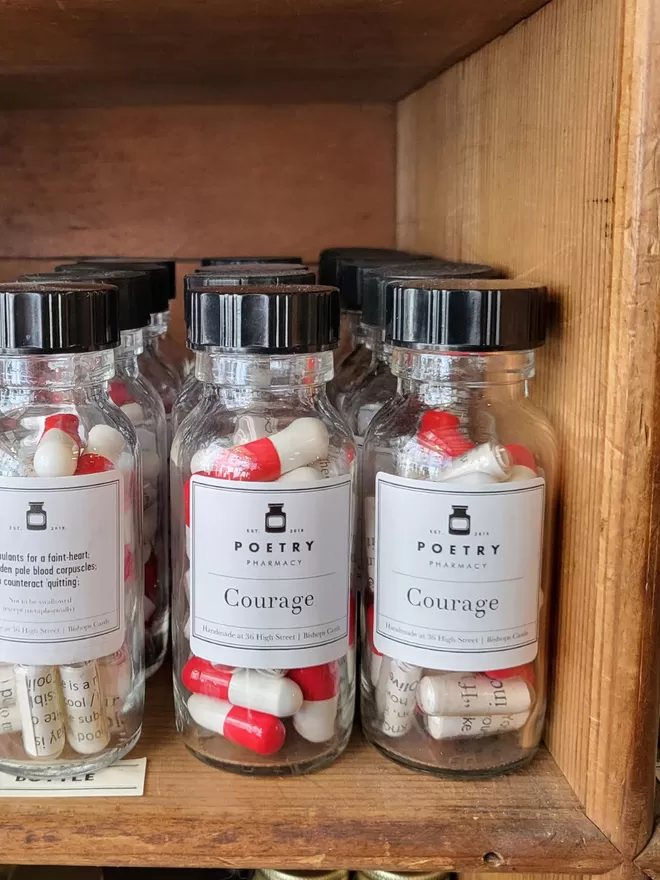 Bottles of red and white Courage poetry pills in rows on a wooden shelf