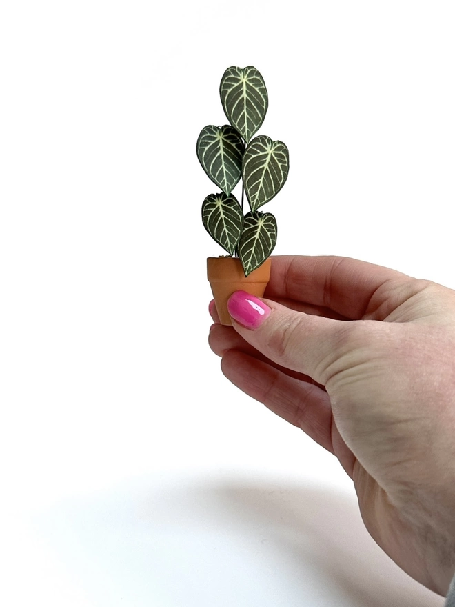A miniature Anthurium Crystal Hope paper plant ornament being held between 2 fingers to show the scale of the plant against a white background