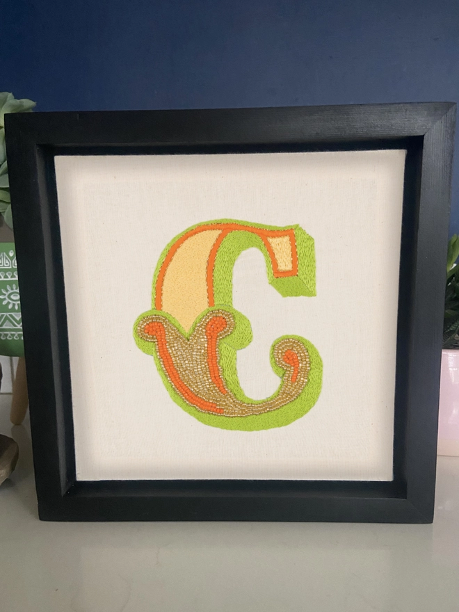 An embroidered and beaded letter C in a box frame