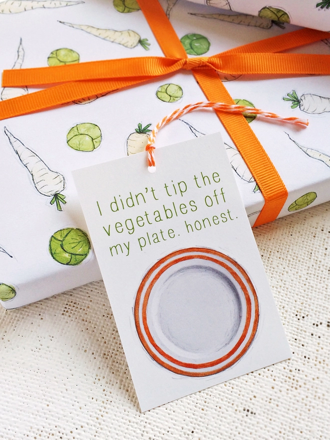 A gift wrapped in fun illustrated sprouts and parsnips wrapping paper is tied with orange ribbon.
