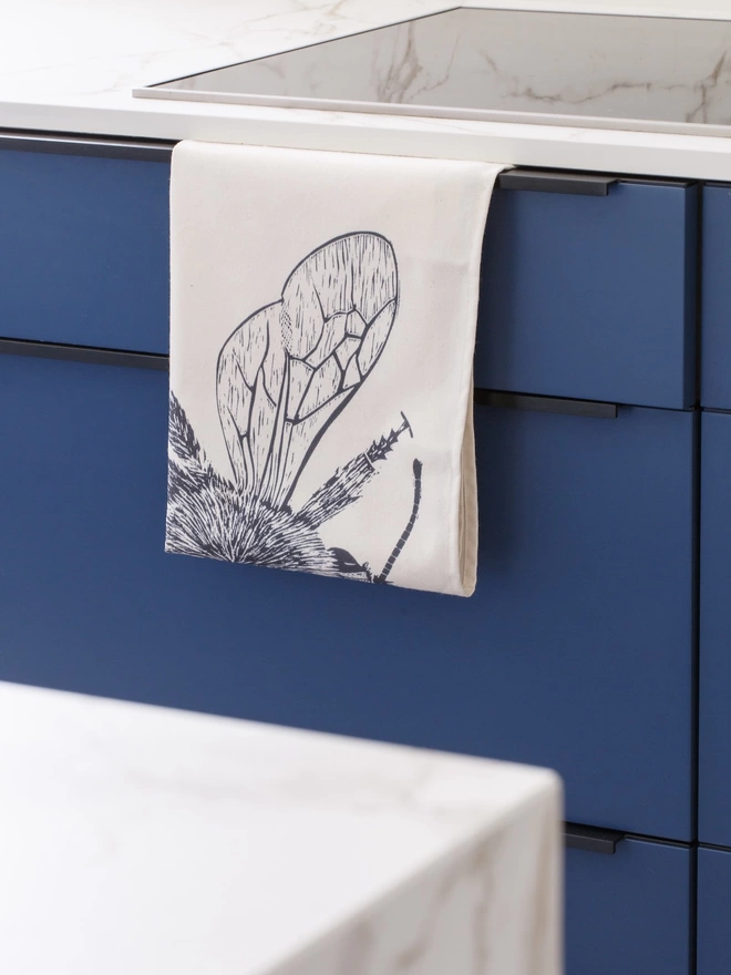 Picture of a tea towel in the kitchen with an image of a bee, taken from an original lino print