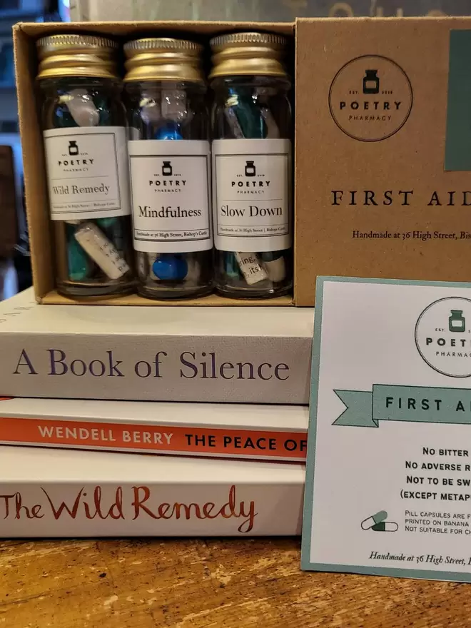 Cardboard box containing 3 glass bottles of poetry pills, and cardboard explanatory insert- displayed on a pile of books