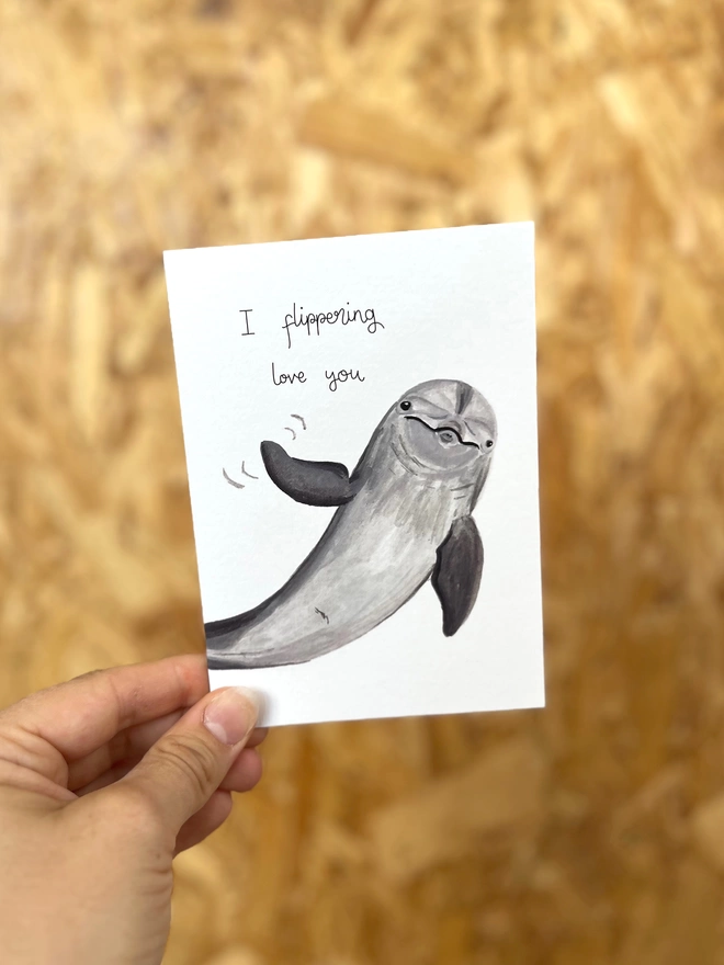 a greetings card featuring an illustration of a dolphin waving its fin with the text “I flippering love you”