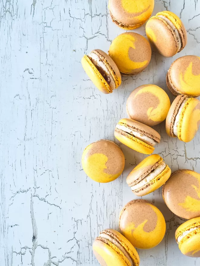 several yellow & brown swirl macarons with caramel oozing out on a white table