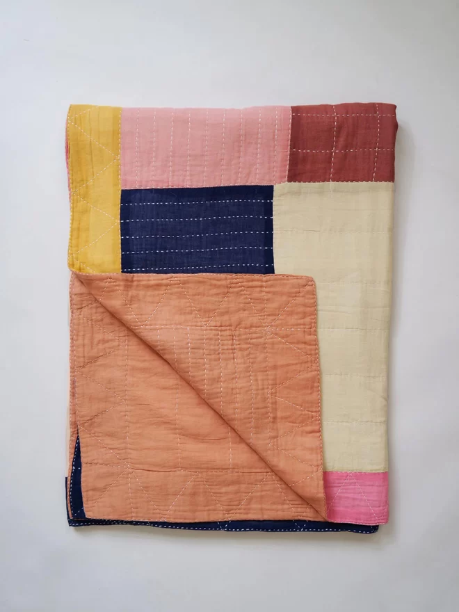 Folded patchwork bedspread in soft tones of pinks, yellow and navy