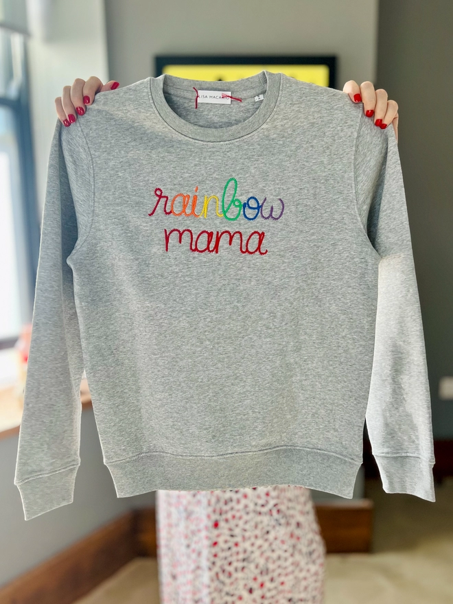 Lisa Macario holding a grey sweatshirt with the words rainbow mama 