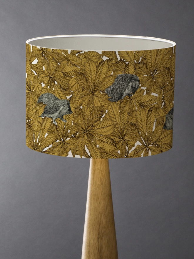 Drum Lampshade featuring hedgehogs in yellow autumn leaves with a white inner on a wooden base 