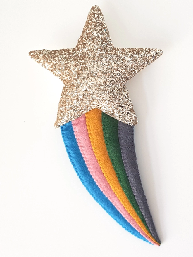 Gold glitter shooting star decoration made from felt. The colours on the tail are dark blue, rose pink, mustard, green and dark grey