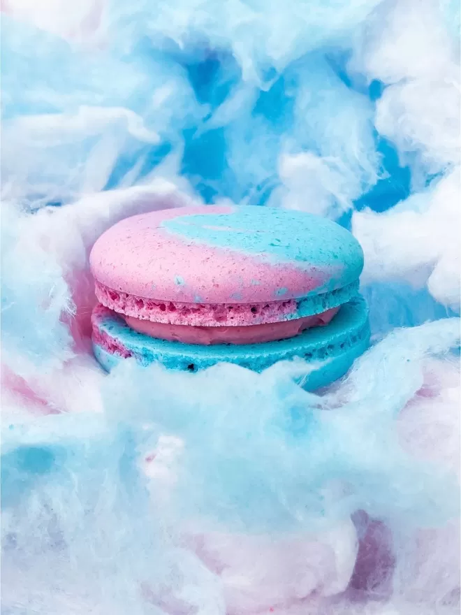a blue and pink macaron sitting on top of a pile of candy floss / cotton candy