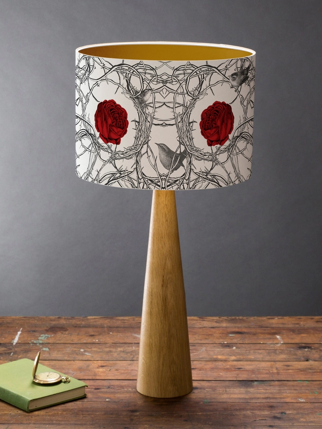 Drum Lampshade featuring red roses in branches with birds on a wooden base on a shelf with books and ornaments