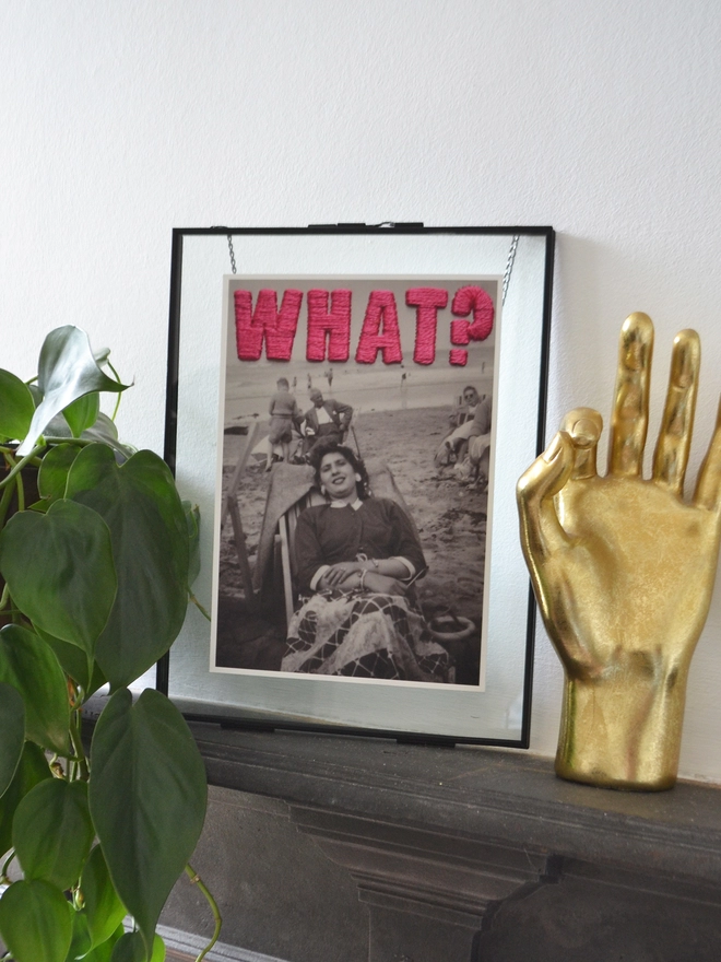  B&W photo print of woman with pink embroidered ‘What?”’ framed on mantlepiece