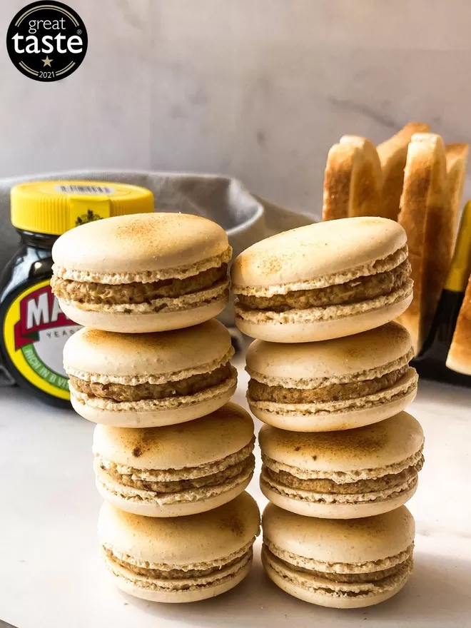several macarons sitting on top of a white table with a jar of marmite and a stack of toast with a great taste award 2021 logo in the top right corner