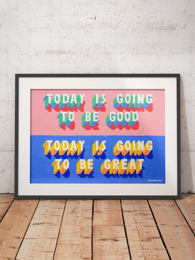Framed art print of words Today Is Going To Be Good Today Is Going To Be Great painted in 3d typography in pink, green, yellow and blue by artist Survival Techniques. Frame leans against wall on wooden floor.