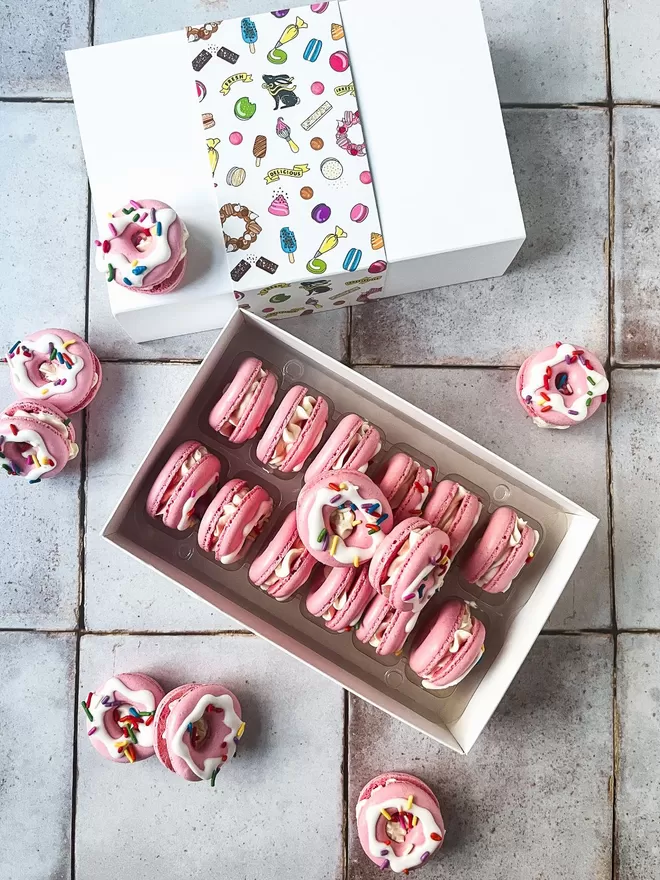 pink doughnut shaped macarons with vibrant & colourful sprinkles in a box on a tiled floor