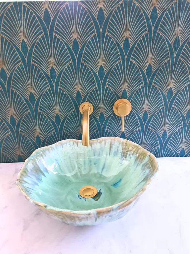 Handcrafted ceramic bathroom basin in a turquoise green blue glaze, hand-crafted sink, pottery basin, wc, bathroom, ensuite, modern bathroom, photographed against green art deco wallpaper with gold taps, homeware, interiors, front view