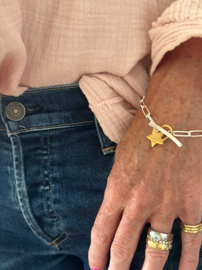 model wears a chunky gold star charm on silver paperclip bracelet with T bar fastener