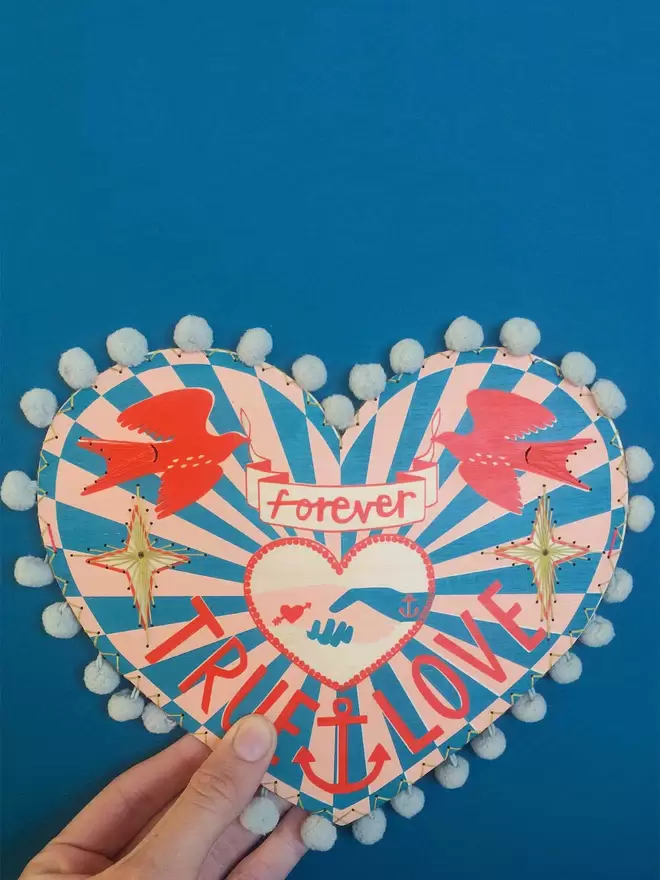 Fiona's hand holds a nautical, colourful wooden screen printed heart, reading 'true love forever'