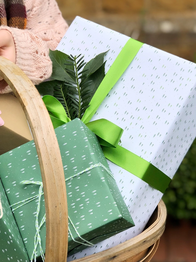 A basket full of gifts wrapped in white and green wrapping paper with a tiny tree design.
