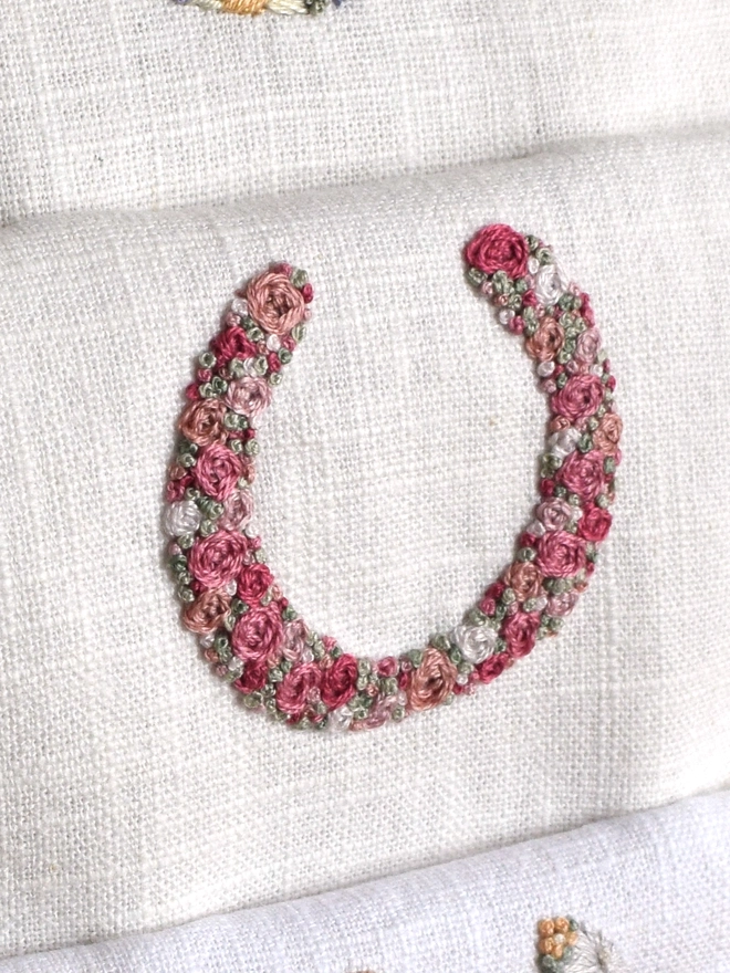 An embroidered Pink Roses Horseshoe, of woven wheel roses in 5 shades of pink with French Knot green grass. 