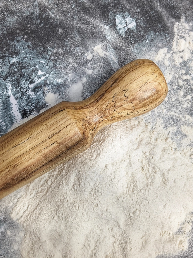 Close up of a stunning hand made rolling pin in Spalted Beech by Something From The Turnery, the picture is focussed on the brown lined all natural detailing along one end of the rolling pin.