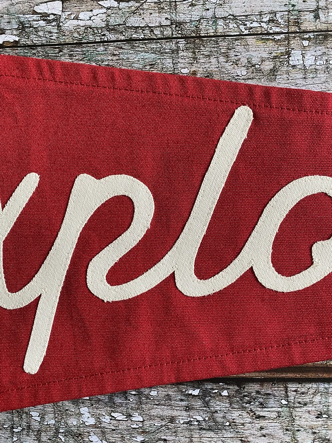 Detail of a red pennant flag showing some lettering of the word Explore written in ivory canvas