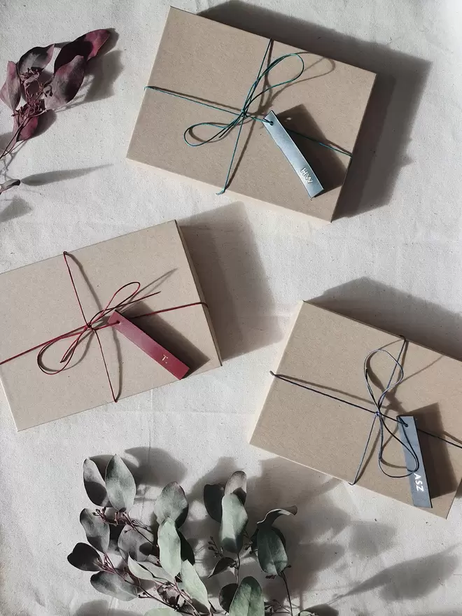 Three wrapped gift sets with leather tags in green, burgundy and grey