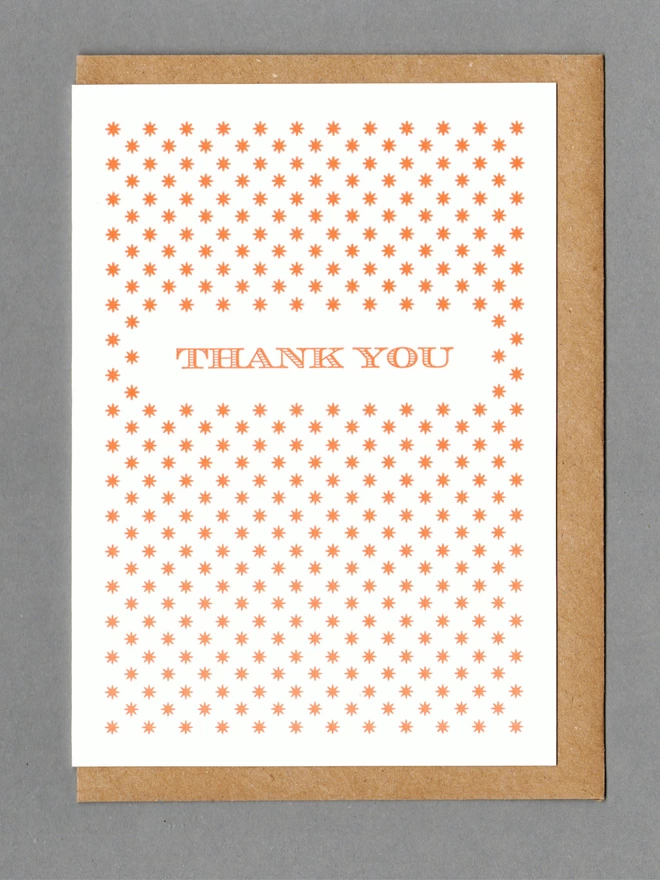 White card with orange stars and orange text reading 'Thank You' with a kraft envelope behind it