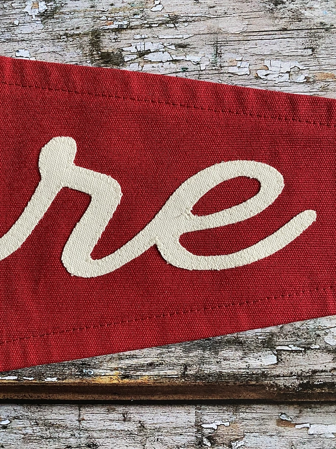 Detail of a red canvas pennant flag showing ivory canvas lettering from the word Explore