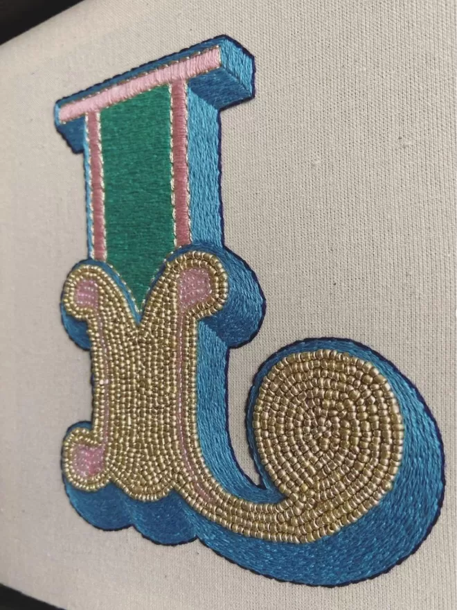 an embroidered and beaded letter L in a box frame