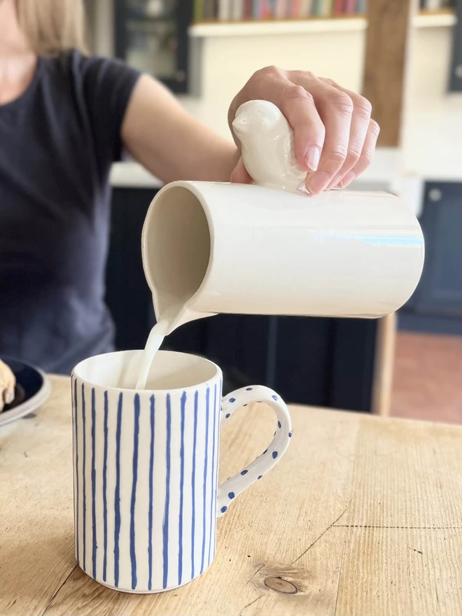 An action shot of a large handmade ceramic bird jug pouring milk into a mug of tea. 