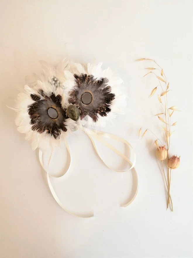 Luxury white masquerade mask laying flat next to dried flowers