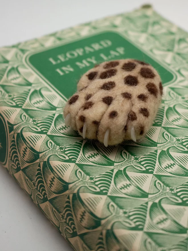 A needle-felted Lucky Leopard Paw on a vintage book with a green pattern