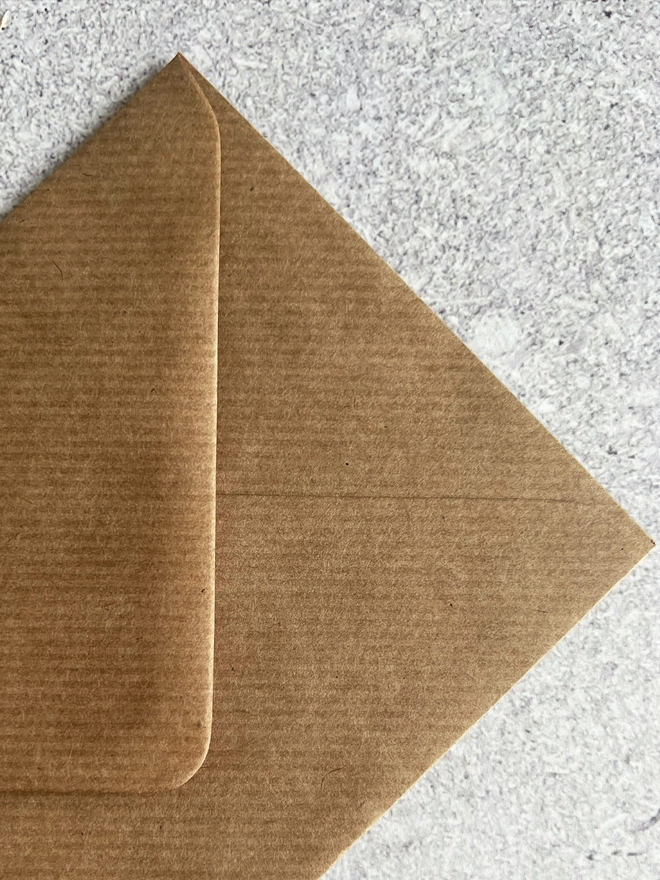 Close up of the lined texture of the brown envelope that comes with this card on a stone background.