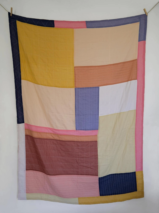 Full view of patchwork quilt in a geometric design featuring different sized squares and rectangles in pink, yellow and blue shades