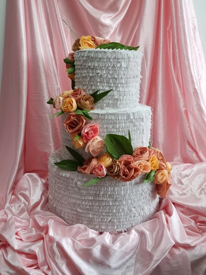 3 tier wedding cake with flowers in muted tones and dark olive leaves surrounded by pink satin drapes