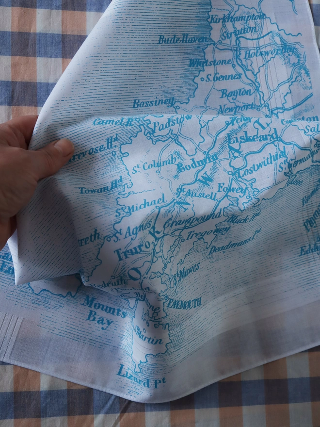 A lifestyle photo of a Mr.PS Cornwall Map hankie printed in aqua being held by a hand.