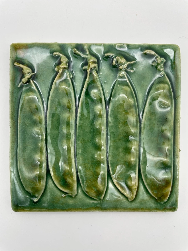 Handmade ceramic tile taken from a plaster cast of real mange tout pea pods, side view. Very realistic, three-dimensional, with lush coloured glazes.